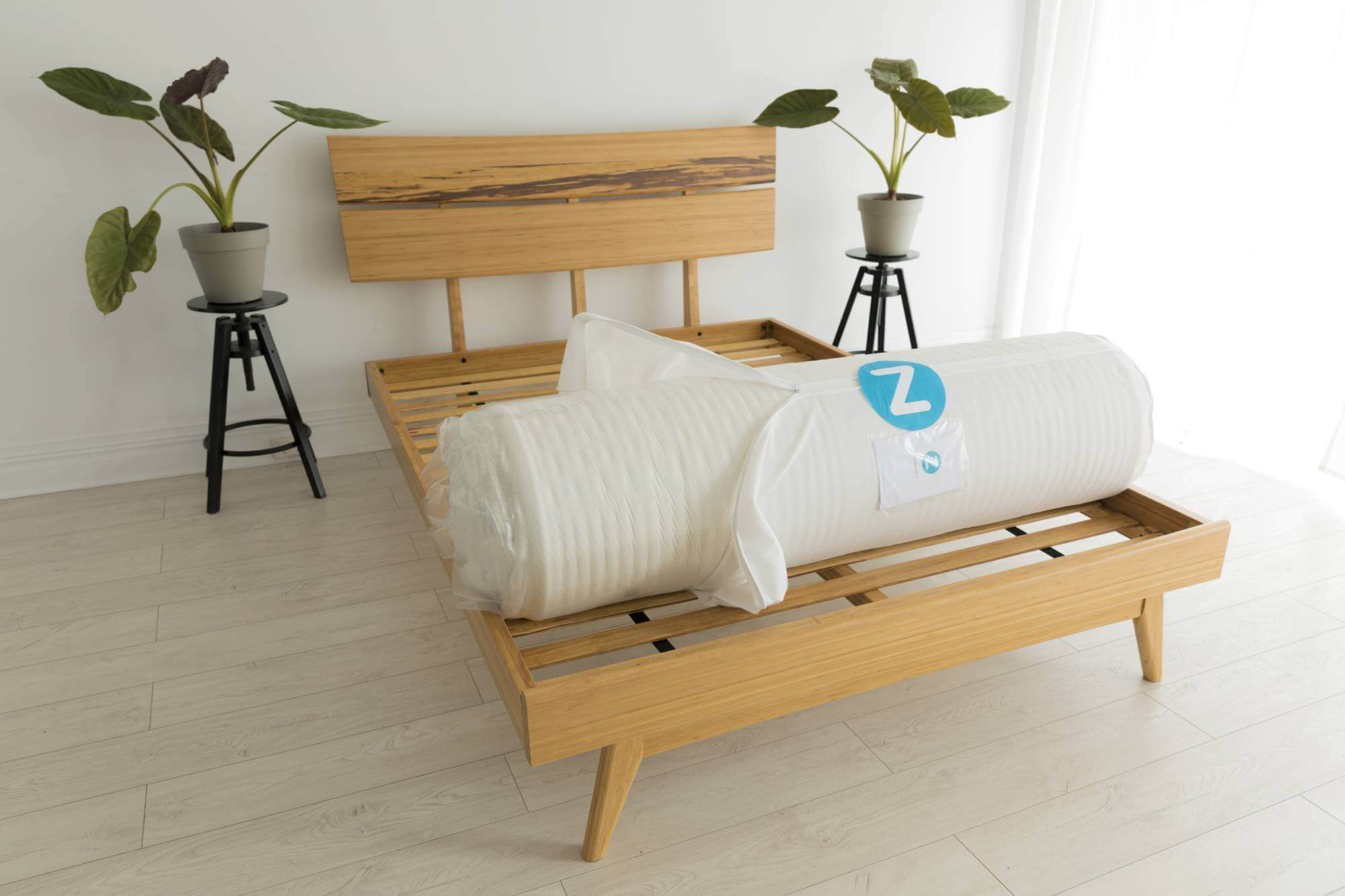 Zenna latex mattress compressed and rolled in waterproof packaging for delivery, on timber bed frame