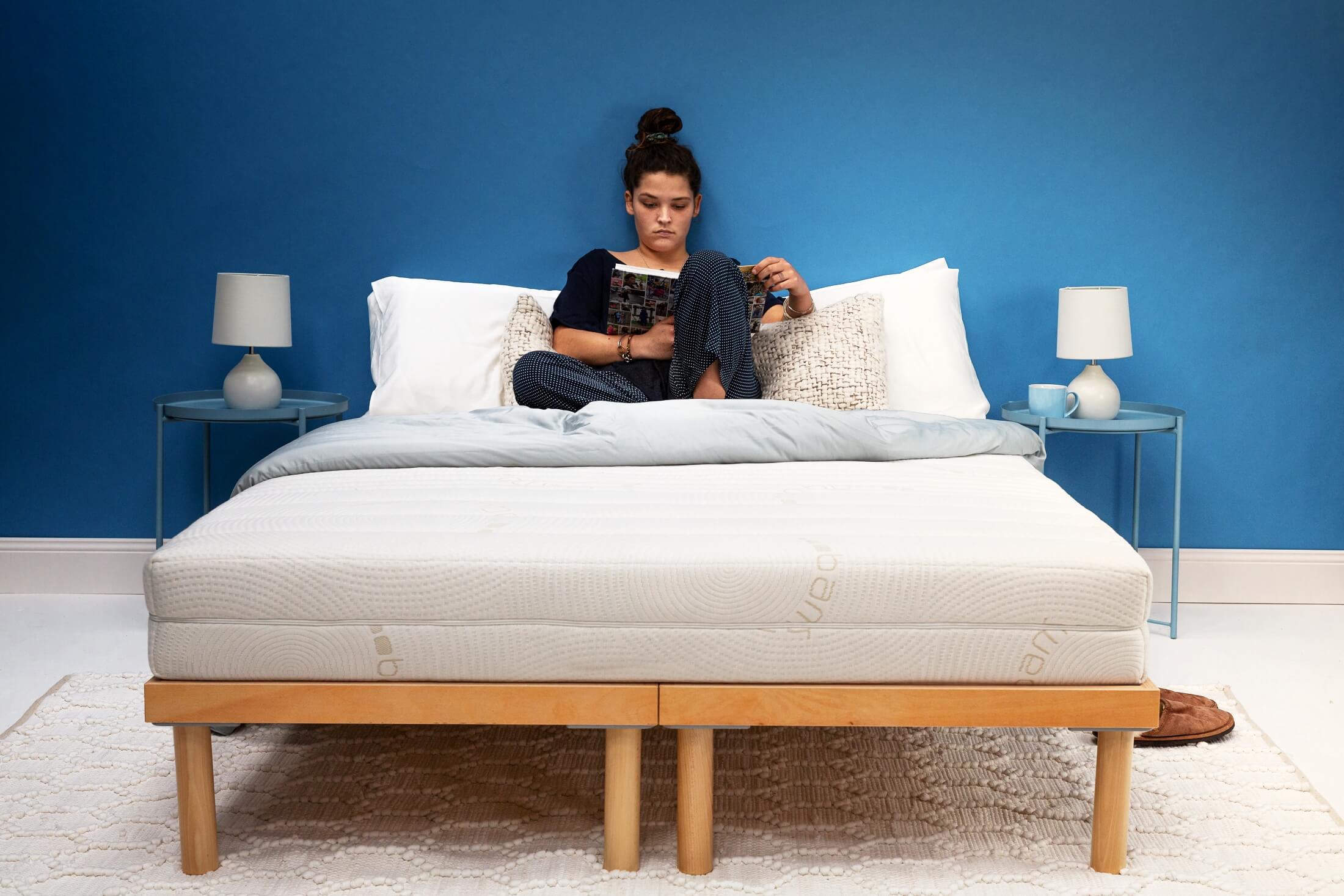 Woman reading magazine on Zenna latex mattress with natural timber bed frame and styled bedroom setting